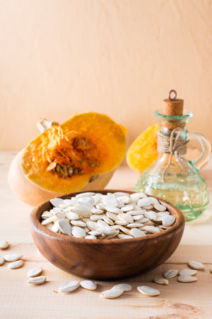 Roasted unpeeled pumpkin seeds in a plate, oil in a bottle and pumpkin pieces on a wooden table. Vertical viewの写真素材