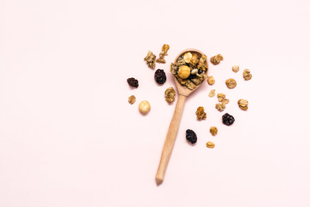 Healthy eating. Baked granola of oats, nuts and raisins in a wooden spoon on a pink background. Top viewの写真素材