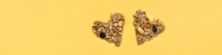 Love for healthy food. Granola made from oats, nuts and raisins in the form of two hearts on a yellow background. Top view. Web bannerの写真素材