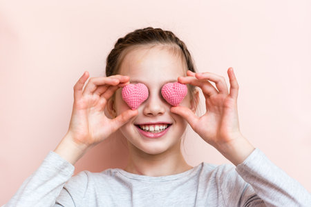 Cheerful smiling girl holding knitted hearts in front of her eyesの写真素材