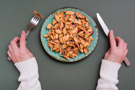 Pieces of dry apples on a plate and cutlery in female hands on a green background. Healthy eatingの写真素材