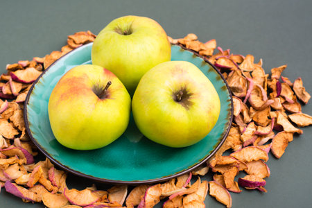 Fresh apples on a plate and pieces of dry apples around on a green backgroundの写真素材