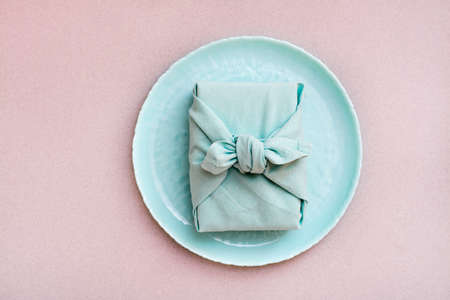 Eco-friendly gift - a box wrapped in cloth on a plate on a gray background. Minimalismの写真素材