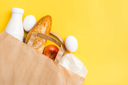 Food delivery concept. Bread, milk, eggs, cereals and fruits in a paper bag on a yellow backgroundの写真素材