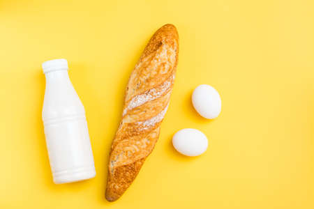 The minimum set of products for breakfast. Bread, eggs and milk on a yellow backgroundの写真素材