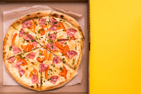 Takeaway and delivery. Ready-to-eat pizza in cardboard box on yellow background. Copy spaceの写真素材