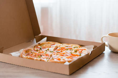 Takeaway food. Pizza in a cardboard box on the table in the kitchen.の写真素材