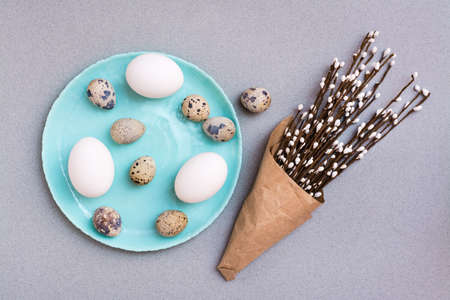 Happy Easter. Chicken and quail eggs on a plate and packaging with pussy willow branches on a gray...
