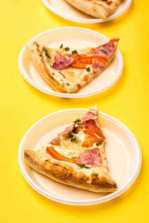 Takeaway and delivery. Three pieces of pizza in disposable plastic plates on a yellow background. Lunch for a group of friends. Vertical viewの写真素材