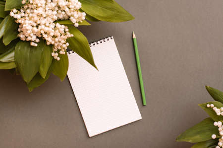 Blank notebook, pencil and bouquets of lilies of the valley on a green background. Top view....