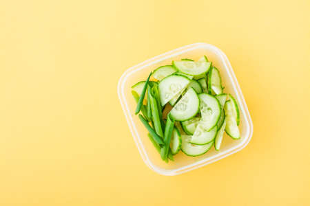 Sliced fresh cucumber and green onions in a box on a yellow background. Takeaway, school breakfast....