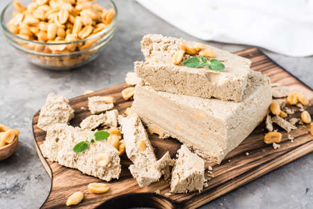 Pieces of sunflower and peanut halva and mint leaves on a cutting board and a bowl of nuts on the...