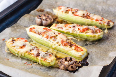 Ready-to-eat baked zucchini halves stuffed with cheese and tomato on baking paper on a baking sheet. Vegetable dishes, healthy foodの写真素材