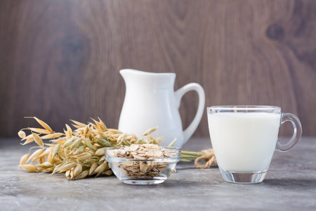 Oat milk in a cup, oatmeal and ears of corn on the table. Alternative to cow's milk