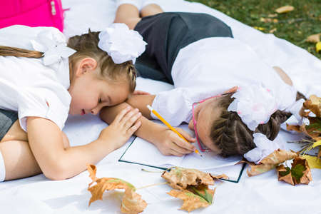 Two cute schoolgirls got tired of doing their homework and fell asleep on a blanket. Outdoor education. Back to school conceptの写真素材