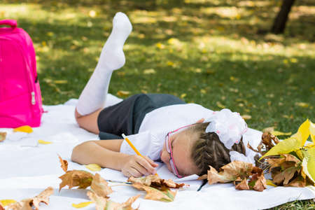 Tired of homework, a schoolgirl fell asleep on a blanket in an autumn sunny park. Outdoor education. Back to school conceptの写真素材