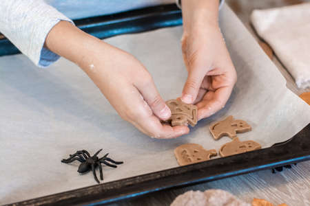 Preparing to celebrate halloween and preparing a treat. Children's hands lay raw halloween cookies on a baking sheet. Lifestyleの写真素材