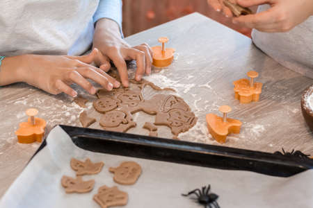 Preparing to celebrate halloween and preparing a treat. Children cut out baking pans for Halloween cookies and a baking sheet of raw cookies on the table. Lifestyleの写真素材