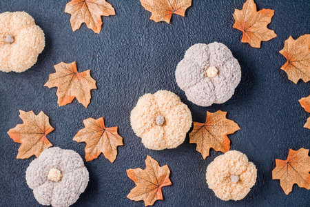 Handcraft autumn still life - knitted pumpkins and maple fabric leaves on a black background. Halloween and Thanksgiving decor. Top view. Copy spaceの写真素材
