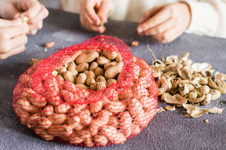 Mesh bag with inshell peanuts and two girls in the background are peeling nuts at the table. Lifestyleの写真素材