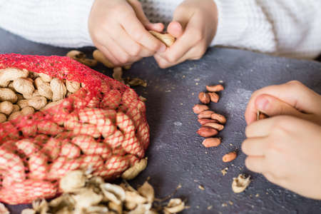 Peanut kernels, a mesh bag with unpeeled nuts and husks on the table. Children's hands are peeling nuts. Lifestyleの写真素材