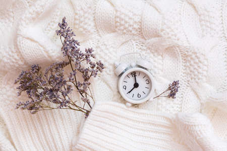 Alarm clock and dry flowers on a cozy white sweater. Wellness time concept. Top viewの写真素材