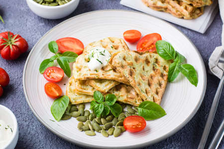 Ready-to-eat delicious zucchini waffles, tomatoes, basil and pumpkin seeds on a plate on the table. Vegetable diet food. Close-upの写真素材