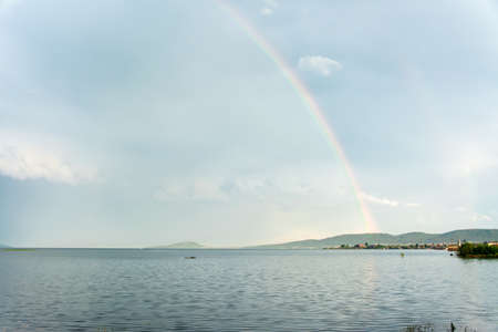 Multicolored beautiful rainbow over the river bay in the sky with clouds. Natural natural phenomenonの写真素材