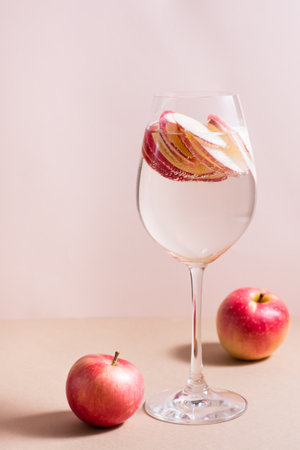 Refreshing cocktail of apple pieces and mineral water in a glass on a pink background. Detox wellbeing drink. Vertical viewの写真素材