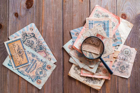 The magnifying glass lies on a pile of old ruble banknotes out of circulation on a wooden table. Study of history. Top viewの写真素材