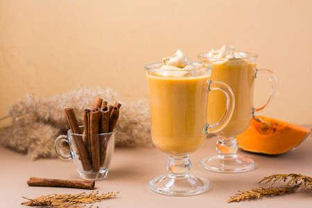 Pumpkin dalgona coffee with cinnamon in glasses on a beige background. Autumn homemade drinks