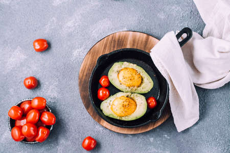 Raw avocado halves, ready to bake, stuffed with egg and cherry tomatoes in a pan on the table. Healthy eating. Flexitarian diet. Top view. Copy spaceの写真素材