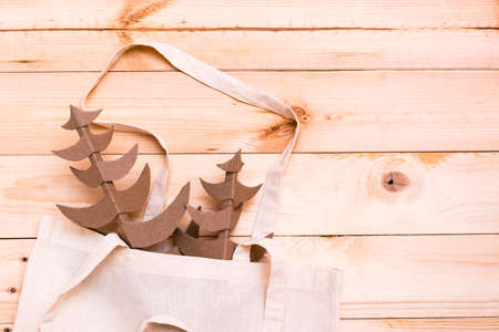 Handmade cardboard Christmas trees in a cotton shopping bag on a natural wooden background. Eco-friendly Christmas conceptの写真素材