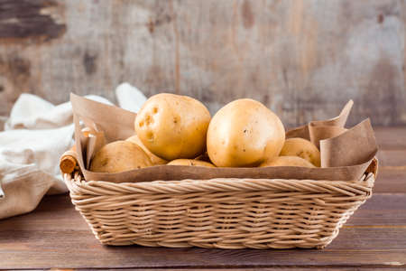 Fresh yellow potatoes in a basket and cloth on a wooden background. Vegetarian food. Close-up. Copy spaceの写真素材