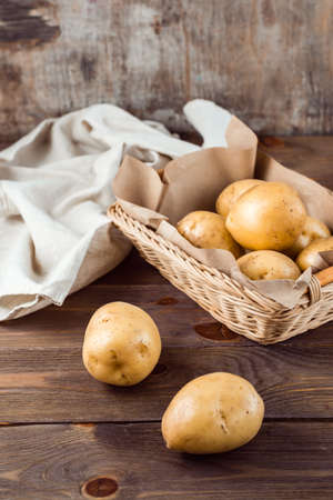 Two tubers of fresh yellow potatoes and vegetables in a basket and on a wooden table. Vegetarian food. Vertical viewの写真素材