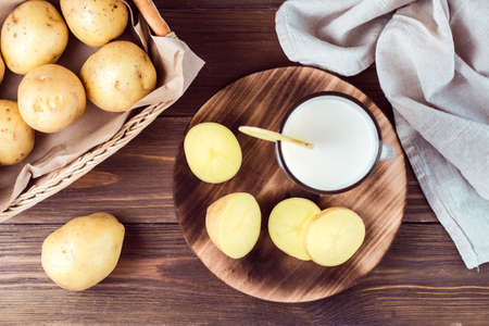 Alternative vegetable vegan potato milk in a glass and potato tubers side by side on a wooden table. Vegetarian food. Top viewの写真素材
