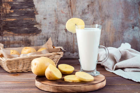 Alternative vegetable vegan potato milk in a glass and potato tubers side by side on a wooden table. Vegetarian food.の写真素材