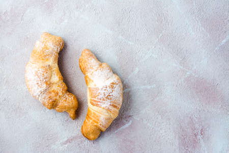 A pair of fresh crispy croissants in powdered sugar on a light textured background. Coffee break or breakfast. Top view. Copy spaceの写真素材