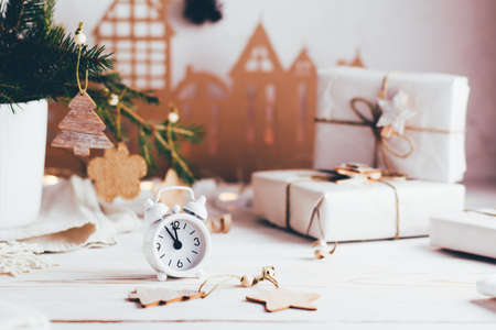 Organization of a festive Christmas table. White alarm clock and gifts in craft paper on the Christmas table. Eco-friendly and homemade lifestyleの写真素材