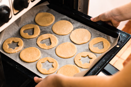 Hands insert a baking sheet of raw Linzer cookies into the oven. Cooking Christmas treats. Lifestyleの写真素材