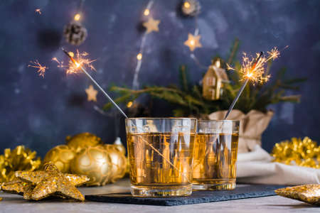 Two glasses with white wine and burning sparklers on the Christmas table. Gold paletteの写真素材