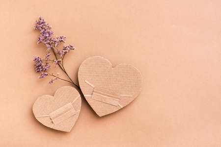 Pandemic date concept. Two masked cardboard hearts with dry flower together on a beige background. Top view. Valentine's dayの写真素材