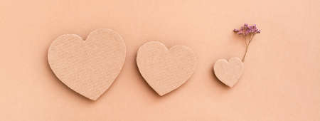 Family concept. Three cardboard hearts - parents and a child with a flower on a beige background. Top view. Web bannerの写真素材