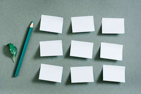 Blank small sheets of paper are arranged in rows and a pencil on a green background. Green concept....
