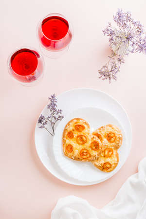 Two heart shaped ready-to-eat pizzas on plates and glasses of wine on a table for valentine's day celebration. Top and vertical viewの写真素材