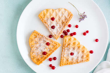 Heart shaped Belgian waffles with red berries and powdered sugar on a plate on the table....