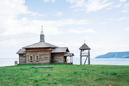 An old wooden log house Russian house and a bell tower on the bank of the river on a summer dayの写真素材