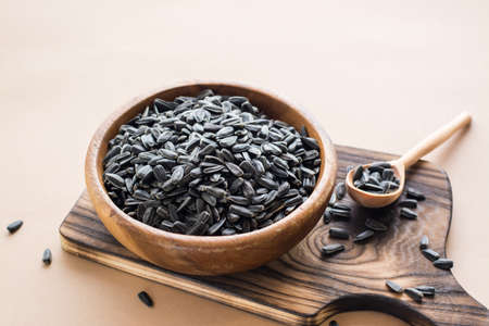Raw unpeeled sunflower seeds in a wooden bowl on a beige background. Natural source of fats and vitaminsの写真素材