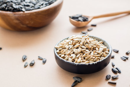 Raw peeled sunflower seeds in a bowl and a plate of unpeeled seeds on the table. Natural source of vitamins and fatsの写真素材