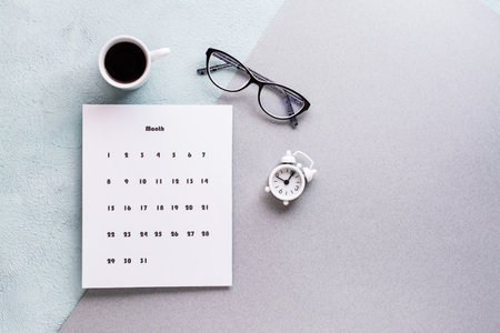 Blank sheet of monthly calendar, coffee cup, alarm clock and glasses on textured background. Time planning and organizationの写真素材